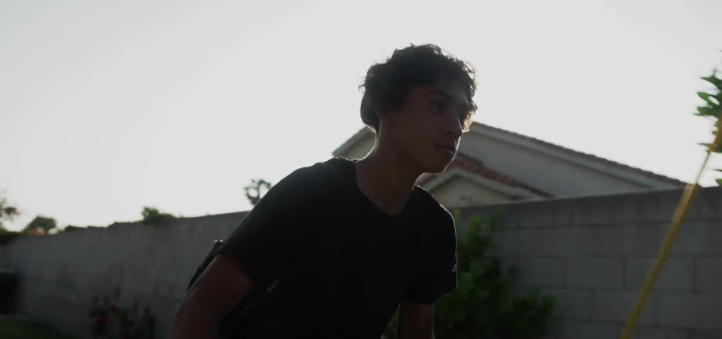 A teenage boy wearing a backpack is riding his bike through a neighborhood