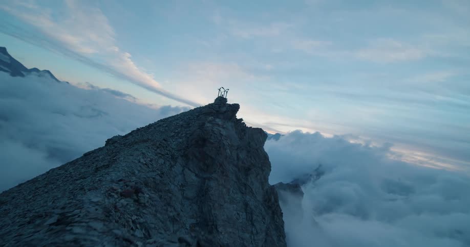 Aerial view of a rough mountain ridge with peaks high above the clouds and a structure on top of the ridge