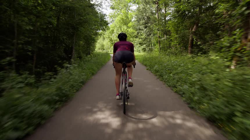 A person cycles through a forest area on a paved road