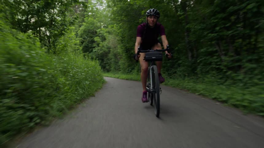 A woman rides a bike down a paved trail through the woods