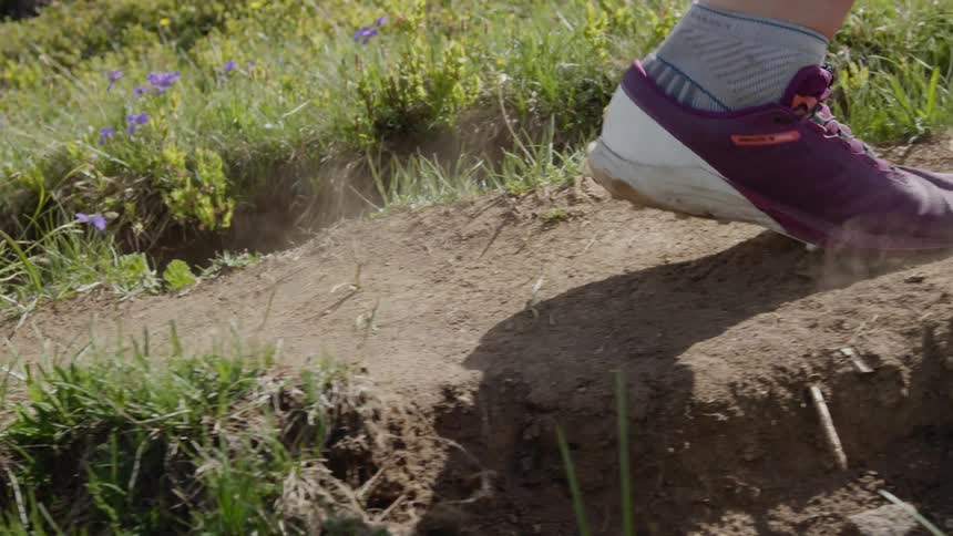A girls feet are seen as she is running on a dirt trail and dust rises when her shoes hit the ground