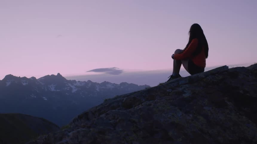 A woman is sitting on a mountain and looking at the horizon