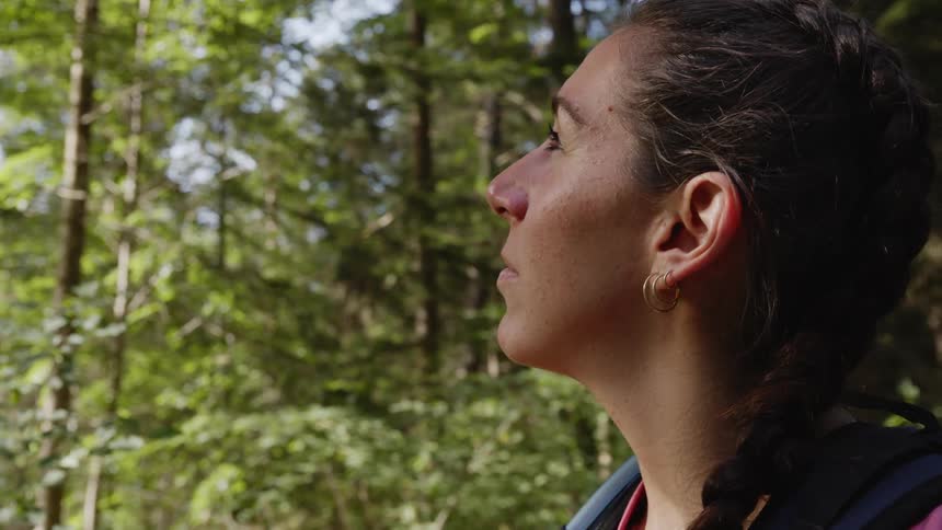 A woman is standing outdoors in a wooded area