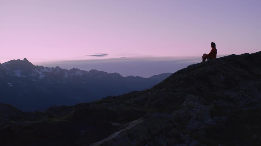 A person is sitting on the mountain and watching the sun set