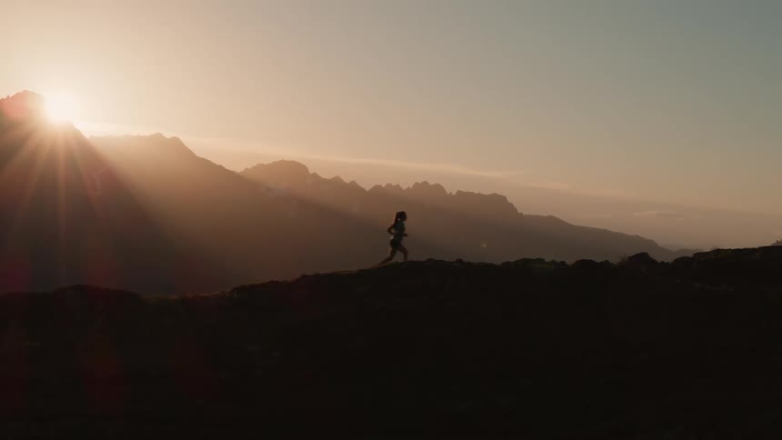 A woman runs through the hills as the sun rises