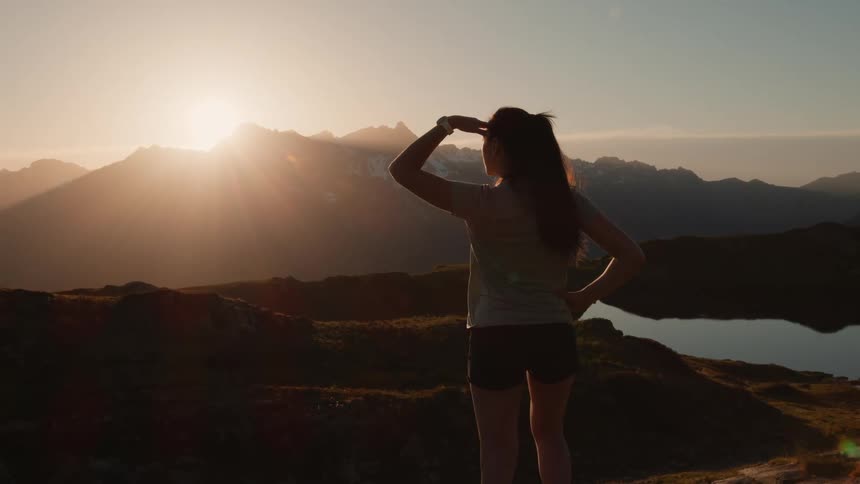 A young white woman is standing up on a hill and looking at the mountains