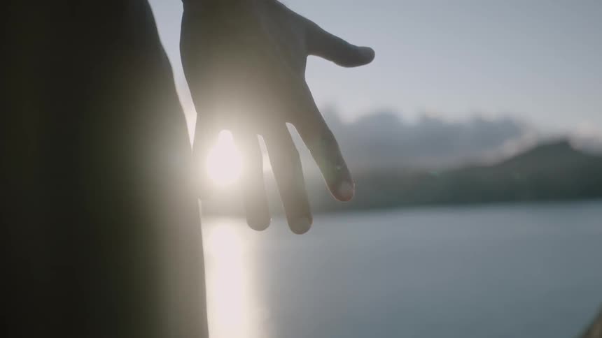 Close-up of a man's hand opening as the sun shines through it at sunset at the beach