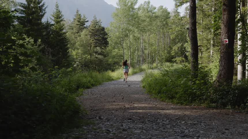 A young white woman is jogging down the road in the forest area