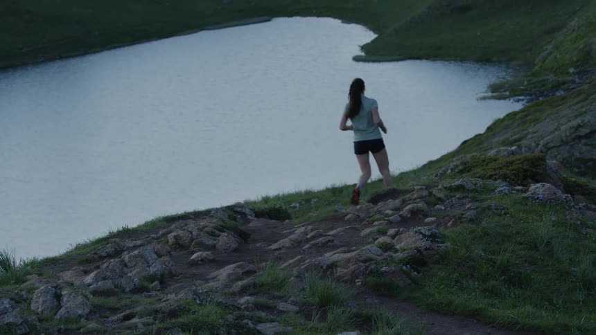 A young white person is jogging down a trail in the woods