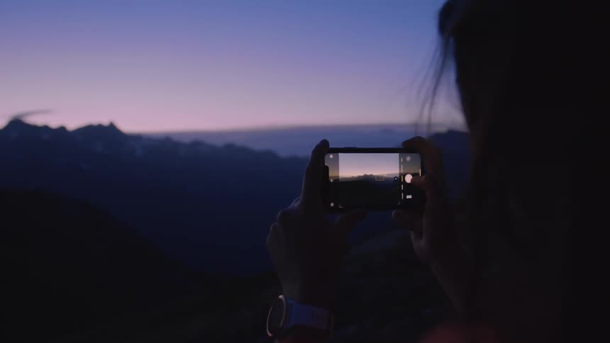 A woman takes a photo of a mountain range on her cell phone at night