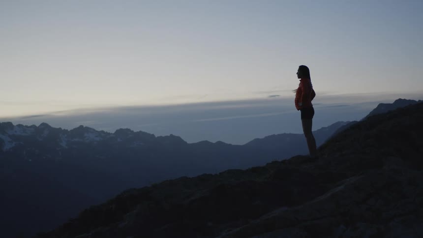 A woman takes in the view from the edge of a cliff on a mountain range