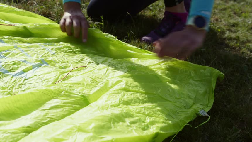 A woman lays out a paragliding canopy on the ground
