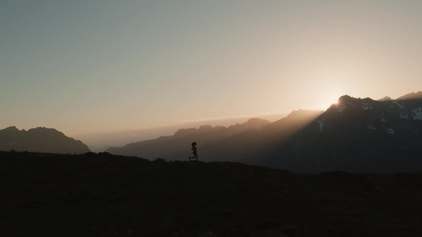 A woman hikes through a mountain range at dusk
