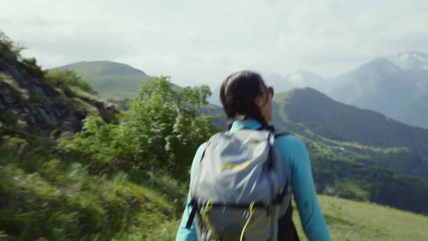 Woman hikes along slope toward mist covered mountains