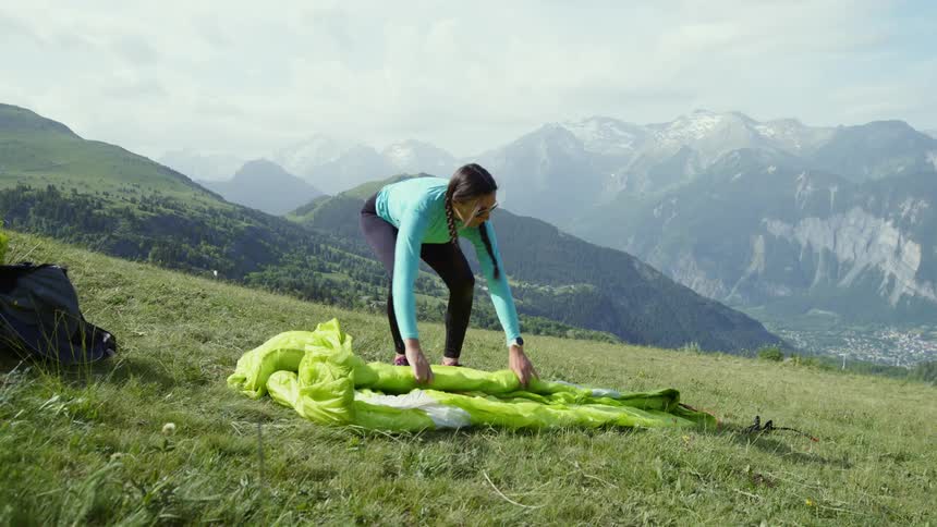 A woman lays out a paragliding canopy on a hill