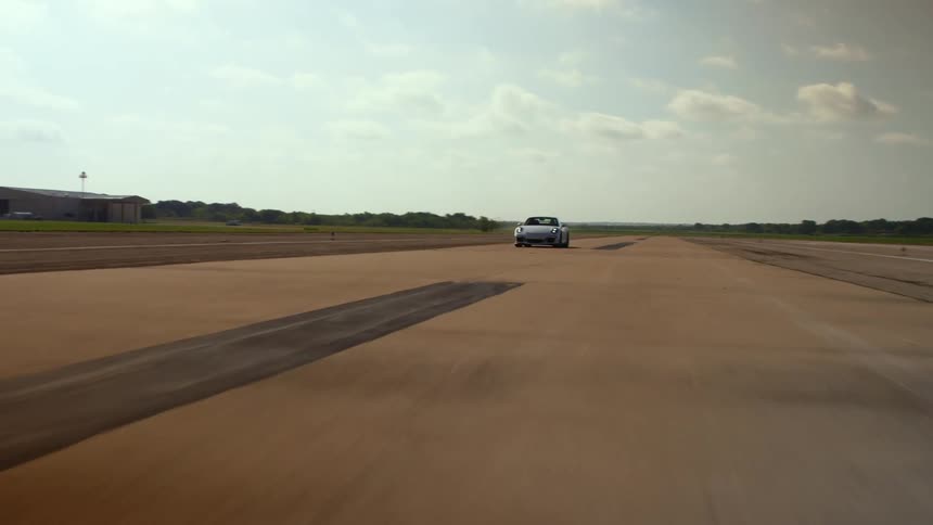 A sports car speeds along a runway in the countryside on a bright day