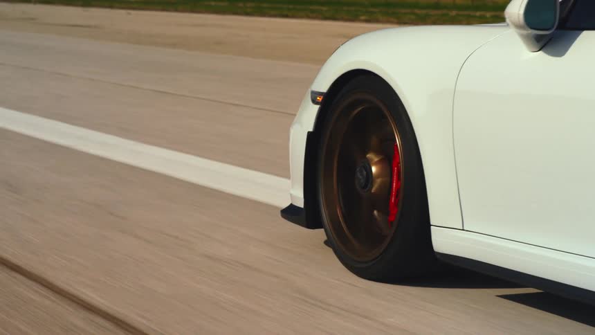 Wheel spins on a white car driving down a road at daytime