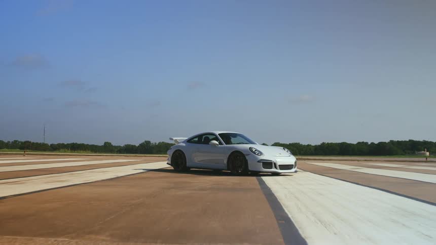 A white porsche parked out on a wide open track at daytime