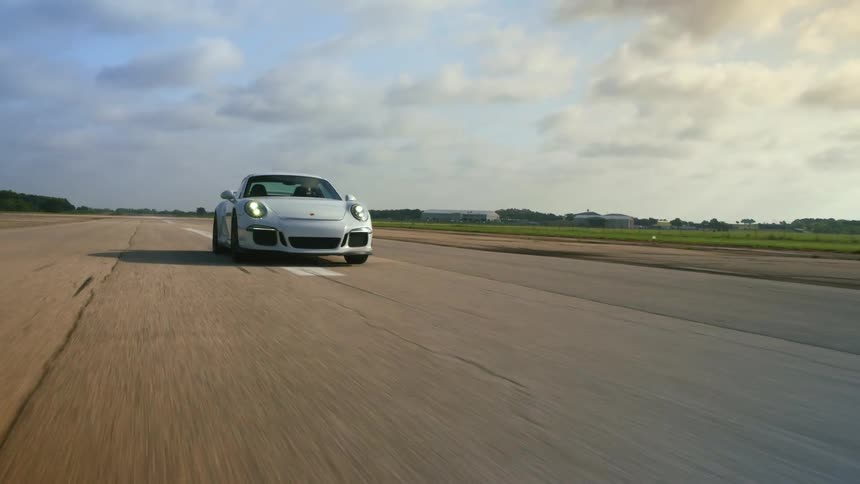 A car driving on a road next to a grassy field with the sky and clouds in the background