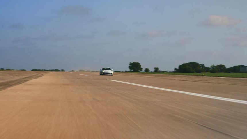 A white porsche car speeds down a race track next to an open field at daytime