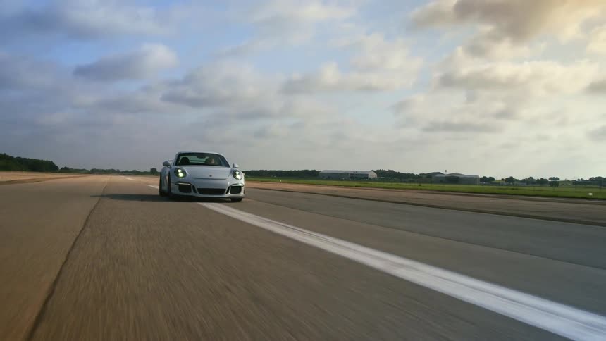 A white porsche driving down a highway strip at daytime