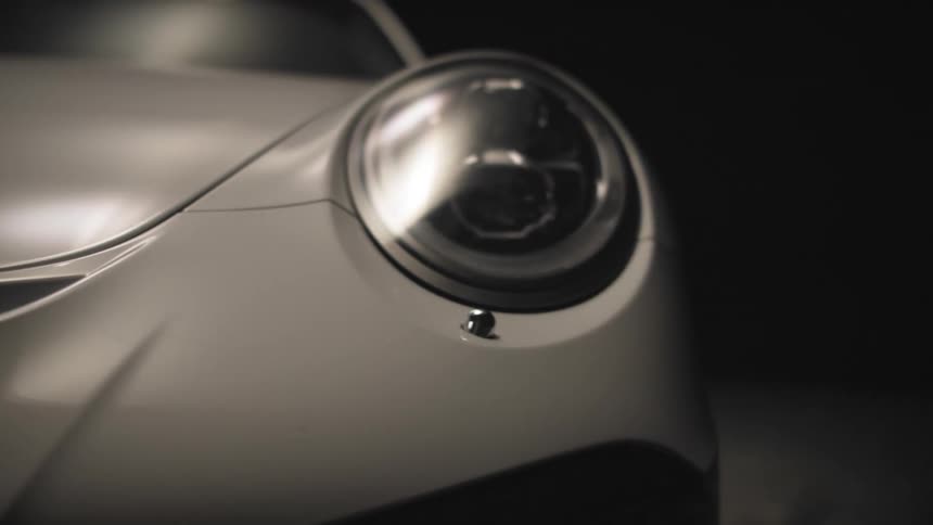 Close up of the front of a white sports car and headlight as it sits indoors