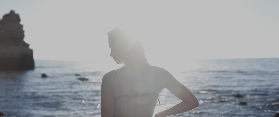 Woman in a bikini standing on the shore at sunset