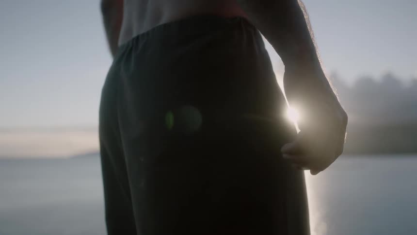 A man standing next to the water at sunset