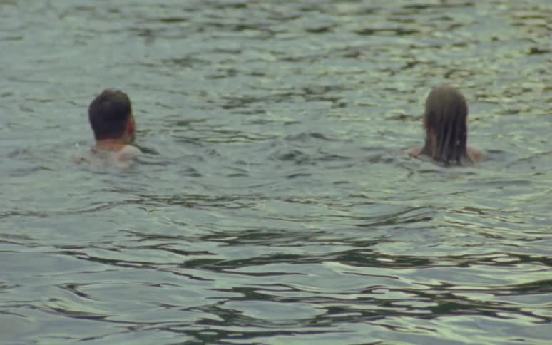 A man and woman swimming side by side away from shore with only their heads above water