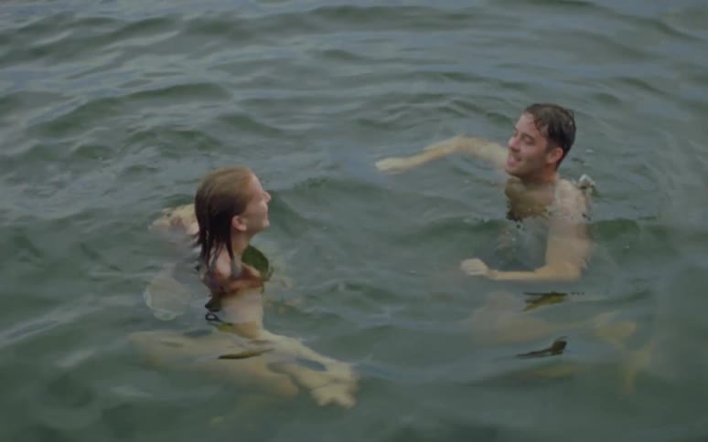 Man wearing black swimming shorts and woman in bikini swim in water