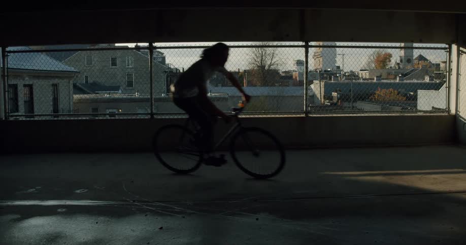 A young man rides a bike on a parking garage level overlooking buildings and homes below