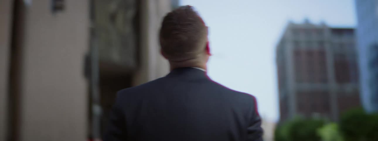 A man walking through a city looks up at high rise office buildings