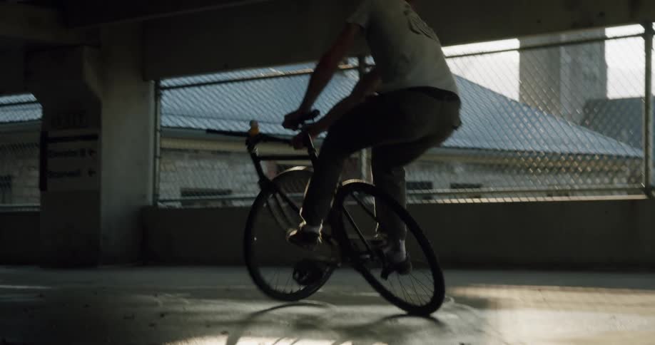 Man in white shirt and green pants does tricks on bicycle indoors