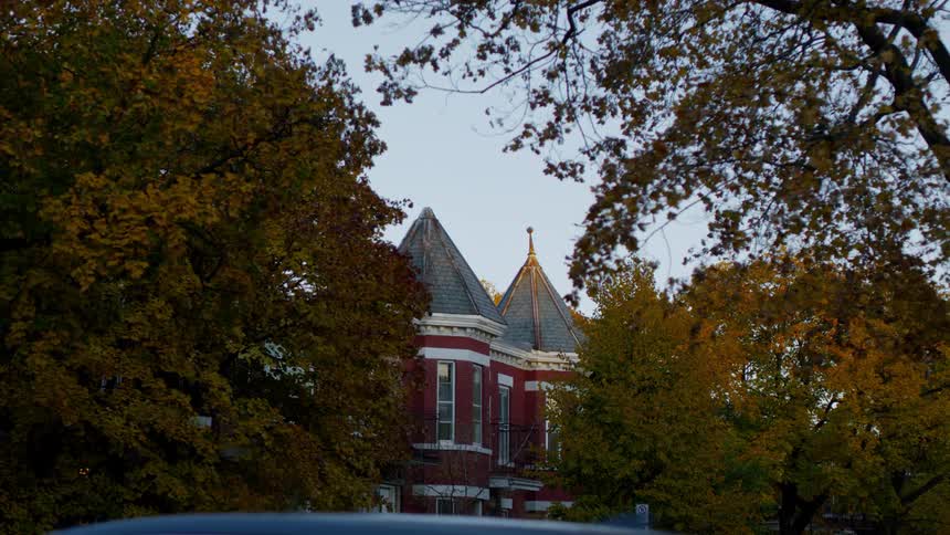 A car drives past a house with trees covered in fall leaves