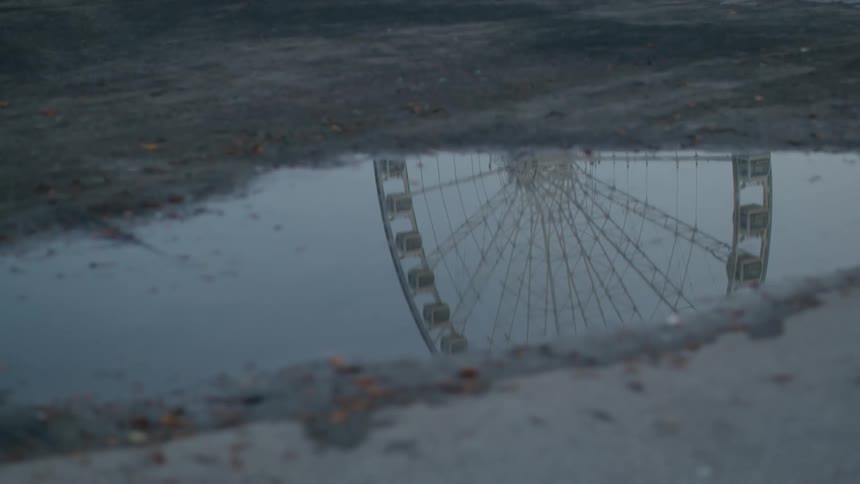A reflection of a ferris wheel in a puddle
