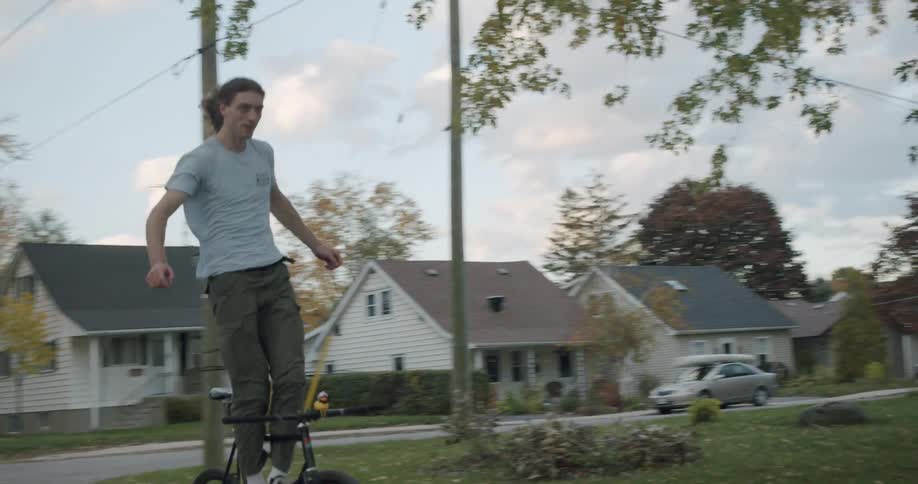 Acrobat standing on the frame of a moving bicycle rides on the street of a calm neighborhood at evening