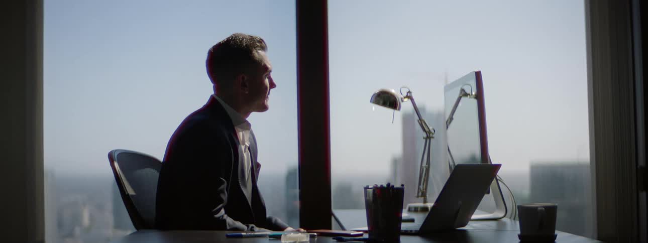 A man is sitting at a desk in an office looking out the window