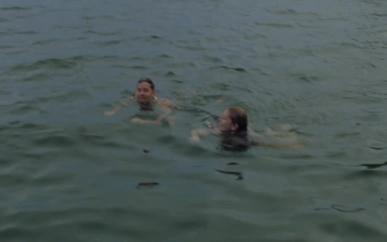 A man and woman swimming side by side talking and smiling at each other