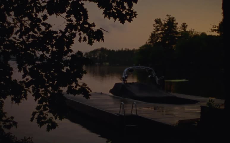 A tarp covered boat next to a wooden dock on a lake at sunset