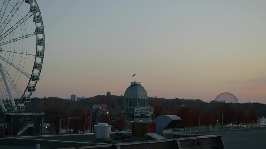 Thick stands of trees separate ferris wheel from city skyline under a red tinted sky
