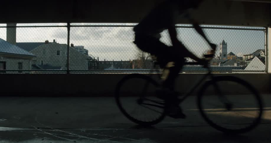 A teenage boy is riding his bicycle in a parking garage and buildings in town are in the distance