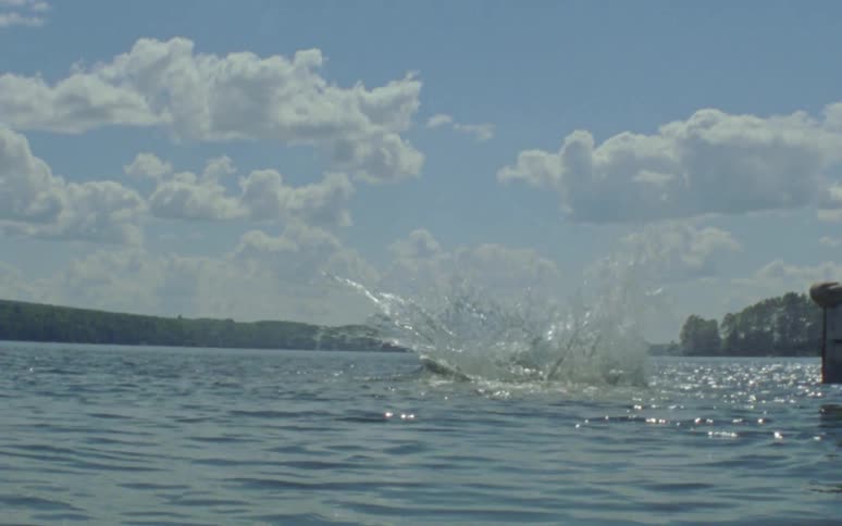 A man jumps twirls and dives off a wooden dock splashing into the lake