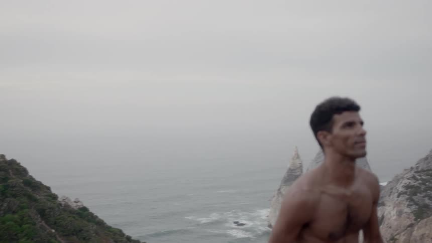Shirtless man climbing a hill next to the ocean
