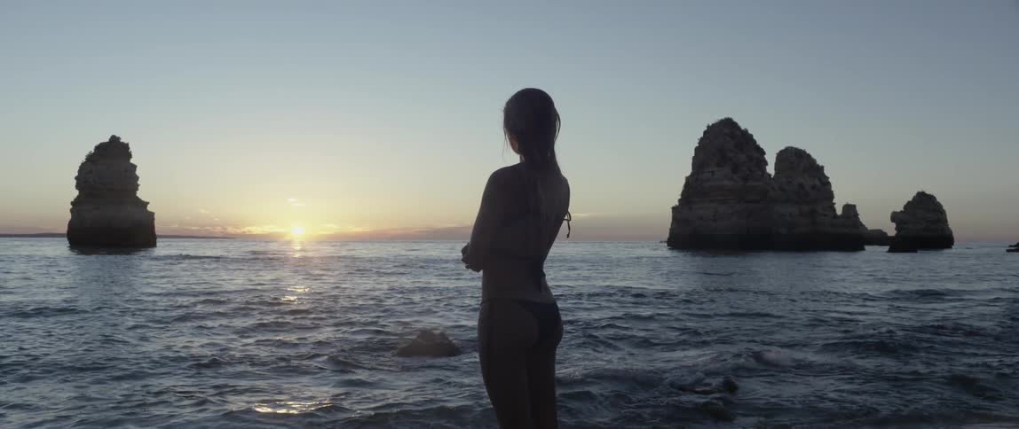 A woman stands by the water watching the sun set