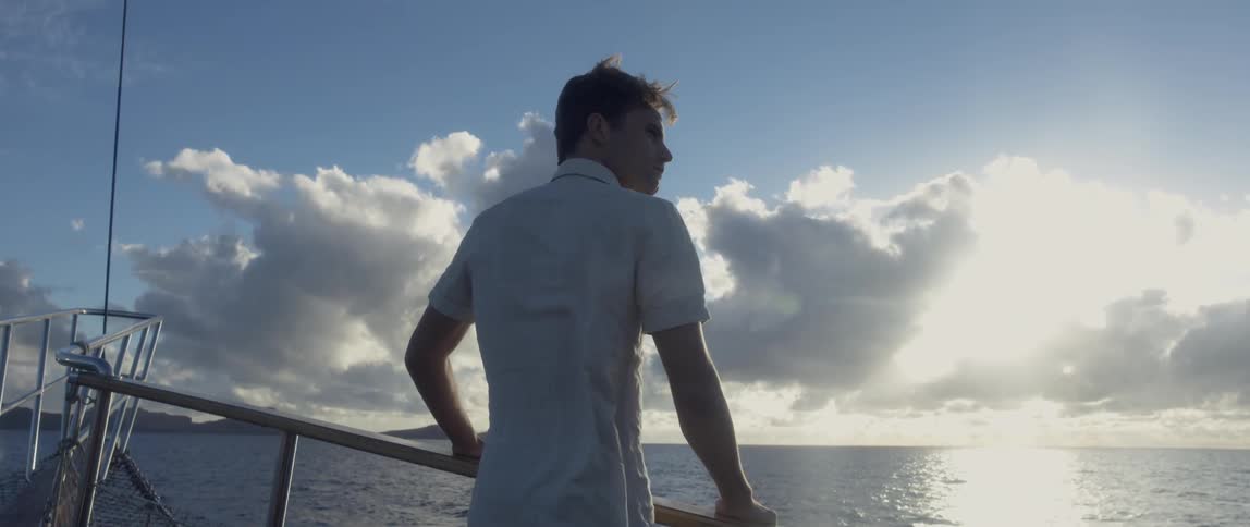 A man leans against the railing of a boat on a windy day