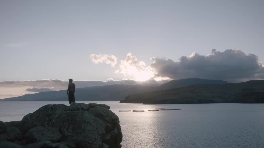 Man standing high upon rocks at a beach area at sunset