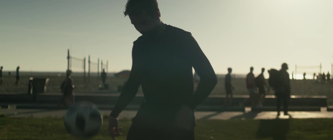 A man juggles a soccer ball with his legs on a beach during the day