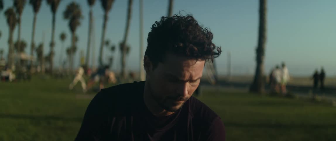 A man in a public park looks off in to the distance as people walk behind him