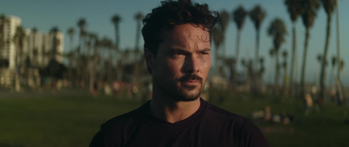 The sun shines on the face of a man standing in a field as people are walking in the distance
