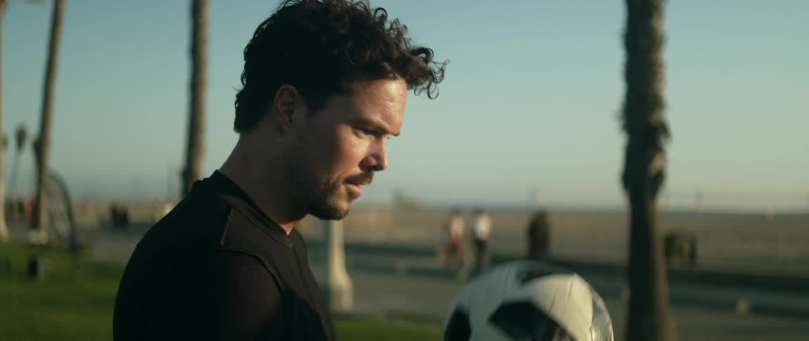 Man in black sweatshirt juggles a soccer ball on lawn near the beach at sunset